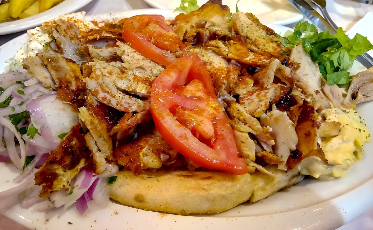 A classic CISSNE'S gyro plate with sliced seasoned meat, fresh vegetables, cool house tzatziki, and warm pita